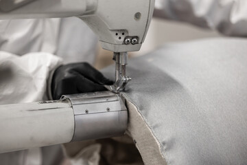 A worker in protective gear uses an industrial sewing machine to stitch heavy-duty fabric. The...