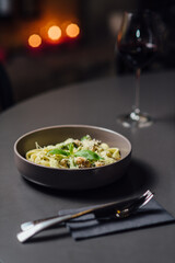 Fettuccine pasta with chicken, broccoli, mushrooms, and grated Parmesan, served on a dark table with elegant cutlery, Vertical composition soft bokeh of candlelit background, paired with red wine