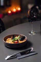Delicious Italian Pasta Dish with Fresh Seafood and Vegetables on a Dark Table. Vertical composition with shallow depth of field, soft bokeh of candlelit background, paired with red wine