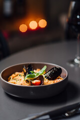 Close up of Italian Pasta Dish with Fresh Seafood and Vegetables on a Dark Table. Vertical composition with shallow depth of field, soft bokeh of candlelit background