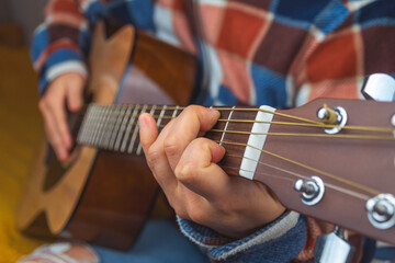 Fototapeta premium a person playing an acoustic guitar, fingers pressing frets, wearing plaid flannel and ripped jeans. Cozy atmosphere