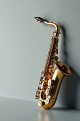 A Gleaming Gold Saxophone Rests Elegantly Against a Smooth Grey Wall, Its Polished Surface Reflecting Soft Light