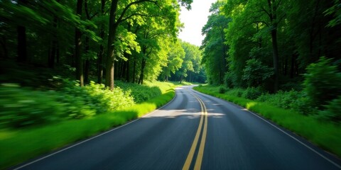 Obraz premium A scenic drive through a lush green forest canopy, a winding road ahead, sunlight filtering through the leaves, motion blur suggesting speed and adventure