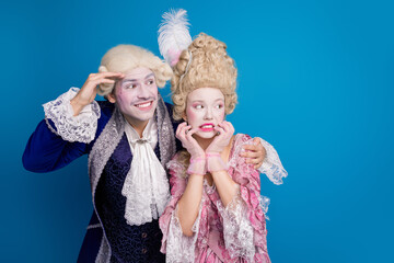 Playful couple in elaborate vintage costumes set against a vibrant blue backdrop, capturing the essence of historical elegance