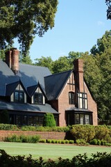 A stunning Tudor-style house is beautifully nestled among lush green trees, basking in the sunshine. The property features a meticulously maintained garden and a perfectly manicured lawn.