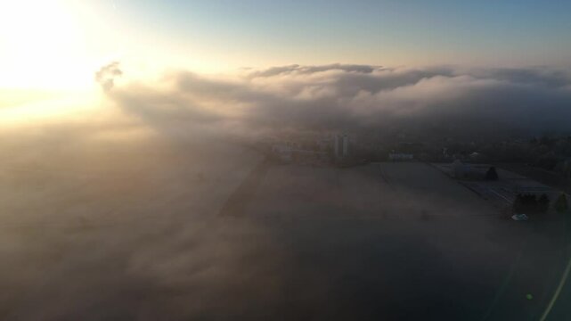Aerial drone footage of sideways flight over countryside and outskirts of a city during foggy sunrise