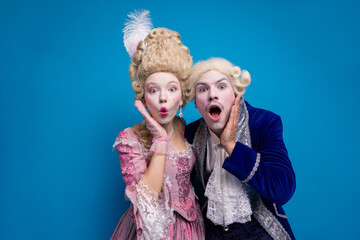 Captivating couple in vintage attire posing playfully against a vibrant blue background.