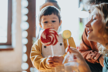 A joyful child engages with a vibrant lollipop while spending quality time with family. The scene...