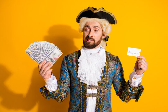 Man in 18th century noble costume creatively illustrating wealth with cash and card against vibrant yellow background