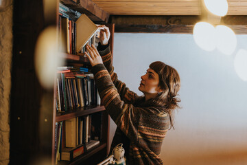 A woman in a warm, rustic setting reaches for a book on a wooden shelf. The ambiance reflects a...