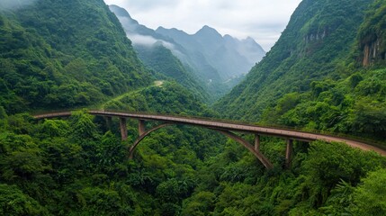 Scenic view of a bridge spanning a lush green valley surrounded by misty mountains