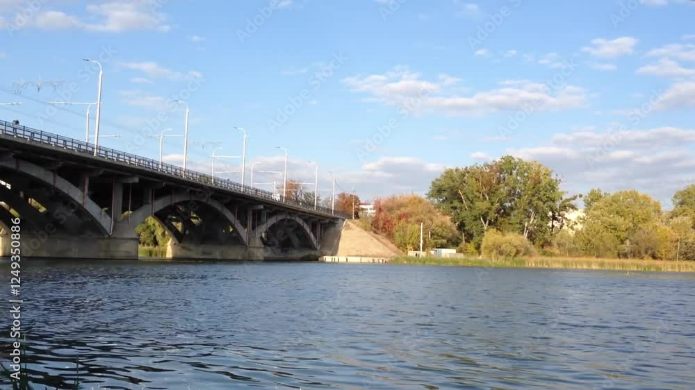 Poster bridge spans a river with a clear blue sky above. the bridge is a large structure with a few trees i