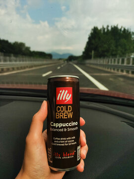 Udine, Italy - July 6, 2024: hand holding cold brew coffee can illy during drive along alpe adria highway, passing verdant landscape in friuli venezia giulia