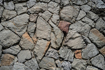 A stone wall with a few large stones and a small one. The wall is made of gray and brown stones