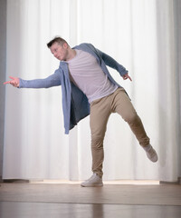 Young guy dancer in motion in a pose. A man performs a modern dance in casual clothes.