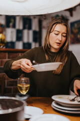 A woman is setting the table while dining in a cozy indoor environment. The atmosphere features warm lighting and a welcoming ambiance, perfect for an intimate gathering or casual dinner.
