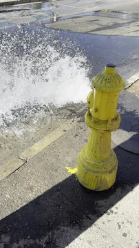 Yellow Fire Hydrant Spraying Water onto City Sidewalk