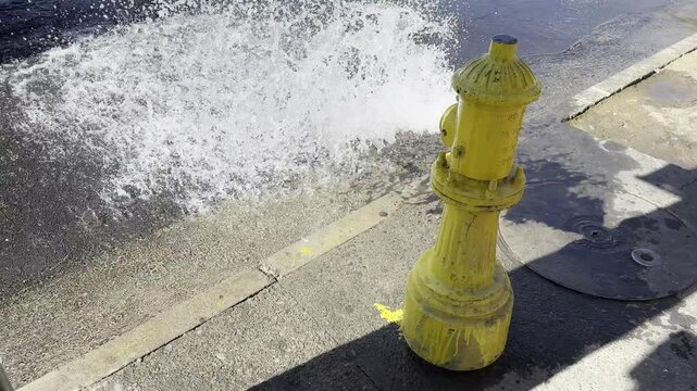 Yellow Fire Hydrant Spraying Water onto City Sidewalk