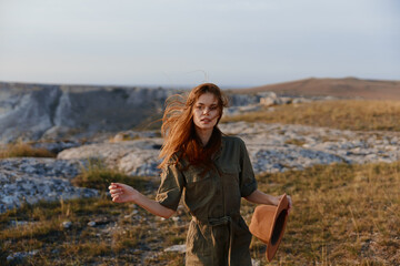 Woman with red hair standing on hill holding hat in hand enjoying beautiful travel view