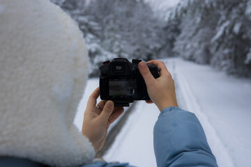 A photographer holds a digital camera and takes pictures of snow-covered trees and a winding path...
