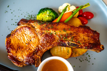 Pork chop with sauce and fried vegetables, potato, tomato, cauliflower, broccoli, asparagus, on white dish in restaurant