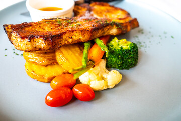 Pork chop with sauce and fried vegetables, potato, tomato, cauliflower, broccoli, asparagus, on white dish in restaurant