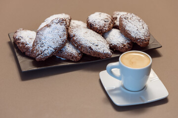 Pan dei Morti cookies with powdered sugar served on a dark textured plate, paired with a white cup of creamy espresso in warm tones