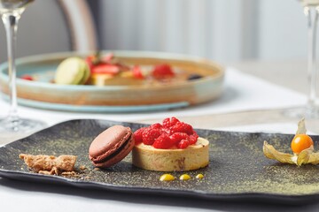 A beautifully crafted dessert featuring fresh raspberries atop a delicate tart, complemented by a macaron, served elegantly at a sushi restaurant. This fine dining experience enchants couples