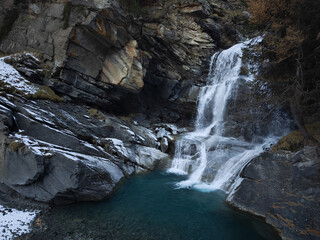 Cascading waterfall tumbling over rocky terrain, surrounded by golden autumn leaves near aosta,...