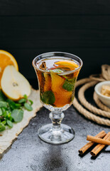 Aromatic herbal tea with citrus, cinnamon, and mint in a glass, set on a dark rustic background
