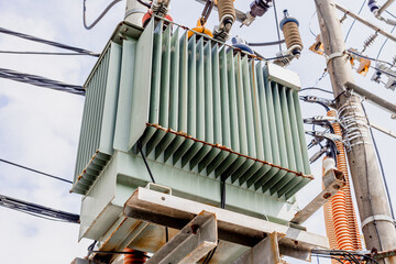 Electric power transformer on utility pole with wires and insulators against blue sky