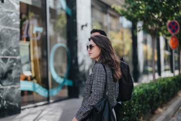 Obraz premium A confident businesswoman wearing sunglasses walks along a city street, exuding professionalism and style. The urban setting adds a dynamic backdrop, highlighting modern business life.