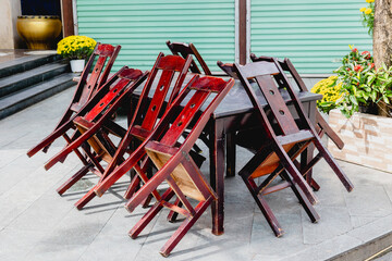 Stacked wooden chairs on outdoor patio with green shutters and floral decor
