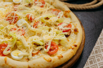 Caesar salad pizza with cherry tomatoes, quail eggs, lettuce, and parmesan, served on a wooden board