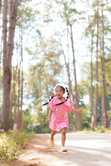 Naklejka premium Asian girl in pink dress running along nature trail with joyful expression. Childhood freedom, adventure, and outdoor learning in natural environment with fresh air and greenery.
