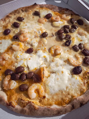Freshly baked shrimp pizza with green olives, melted cheese, highlighting traditional italian flavors. Photographed in aosta during autumn