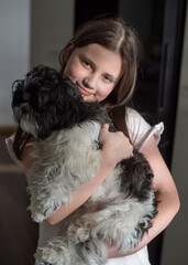 A girl in a white outfit hugging her small black and white dog on a cozy bed.