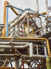 Complex network of industrial metal pipes under cloudy skies.