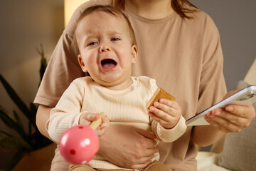 A young child sits on their caregiver's lap, visibly upset and crying. The toddler holds a pink toy...