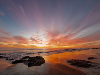 Obraz premium Dramatic sunset on the beach with wispy clouds and reflections on the sandy beach
