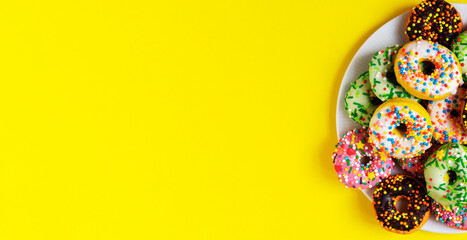 Colorful donuts on a white plate on yellow background