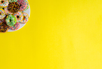 Colorful donuts on a white plate on yellow background