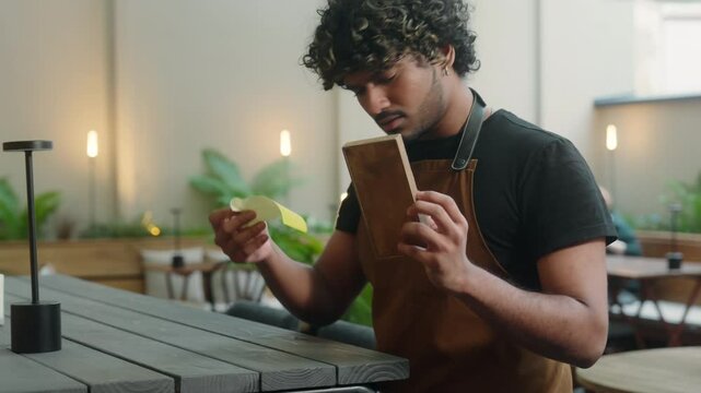 Upset sad Indian Arabian latino man waiter in apron guy cleaner cafe worker male business owner barista serving in cafe no money cash tips bad service in restaurant bill payment dissatisfied worried