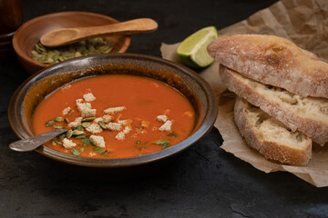 Vegan roasted pepper and tomato soup along with chiabatta bread on dark backround