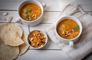 Vegan pumkin and spice soup garnished with peanuts and crackers on white wooden table