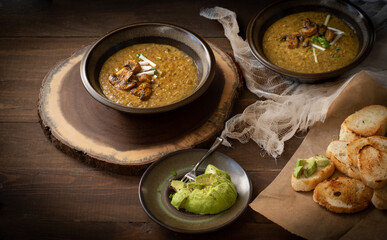 Vegan cream of mushroom soup on wooden table along with toasted bread and avocado