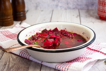 Beet soup in enameled bowl on wooden table, rustic setting