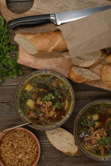 Beet greens and potato soup with bread and crispy onion, wooden background