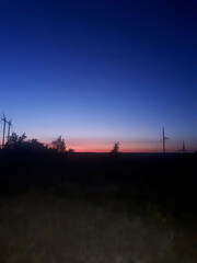 Colorful sunset over silhouettes of trees and power lines in a rural landscape