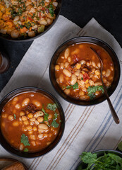 Vegan bean and garbanzo soup along with salad bowl served in black bowls on dark backround